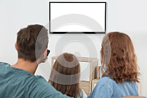 Family with remote control sitting on couch and watching TV at home, space for design on screen