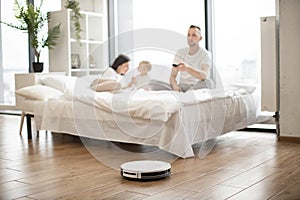 Family resting on bed while using robot vacuum cleaner