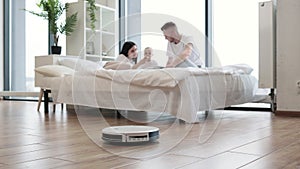 Family resting on bed while using robot vacuum cleaner