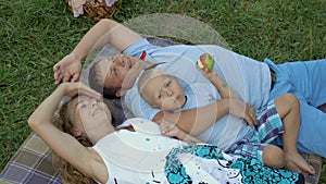 Family resting in nature. Mom, dad and little son lie on the grass on a blanket, hugging and looking at the sky. Boy