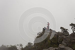 A family resting over a big old stone used as a viewpoint in middle of rainforest with a dense fog