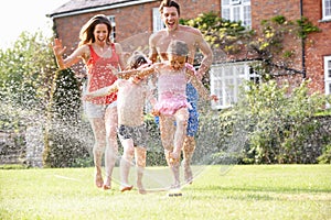 Family Running Through Garden Sprinkler