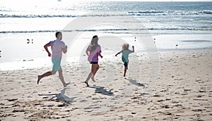 Family running on a sandy beach. Concept of friendly family jogging outdoors. Active parents and people outdoor activity