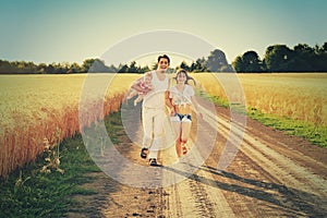 Family Running Together Through Summer Harvested Field. Happy family enjoying and running together outdoors.