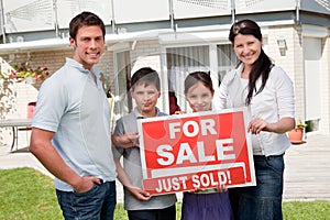 Family with a sale sign outside their new home