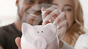 Family Savings, Happy Multiracial Couple Putting Coin In Piggybank Indoors
