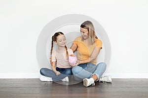 Family Savings. Happy Young Mother And Cute Little Girl Holding Piggy Bank