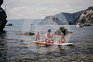 Family sea sup. Young happy father with his son and daughter Floating on a SUP board, paddling in blue sea water. summer