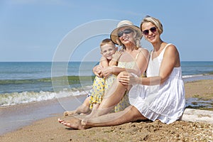 Family on the seashore. A young woman in a white sundress, an elderly woman in a yellow dress and a boy in shorts are laughing and