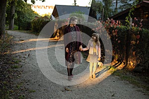 Family, season and people concept - happy mother and little daughter walking along autumn park by the road in the village