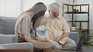 Family senior grandfather, daughter and granddaughter talking online via video chat using laptop computer