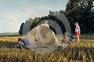 Family set up tent camp at sunset, beautiful summer landscape. Tourism, hiking and traveling in nature