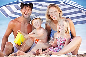 Family Sheltering From Sun Under Beach Umbrella
