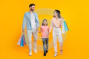 Family shopping concept. Happy caucasian parents and daughter carrying shopper bags, yellow background, full length