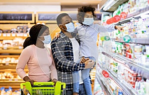 Family shopping during coronavirus pandemic. Black family with child wearing face masks, purchasing food at supermarket