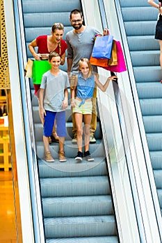 Family in shopping mall on escalators with bags