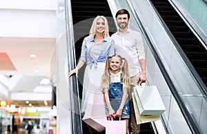 Parents And Daughter Holding Shopping Bags Using Escalator In Mall