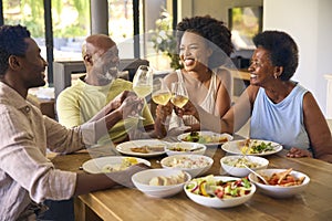 Family Shot With Senior Parents And Adult Offspring Around Table At Home Doing Cheers Before Meal