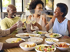 Family Shot With Senior Parents And Adult Offspring Around Table At Home Doing Cheers Before Meal