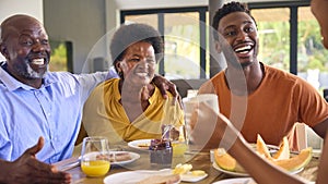 Family Shot With Senior Parents And Adult Offspring At Breakfast Around Table At Home