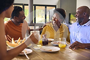 Family Shot With Senior Parents And Adult Offspring At Breakfast Around Table At Home