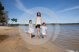 family of single mother, and two child, son daughter walking holding hands in the sea sand of a sunny beach