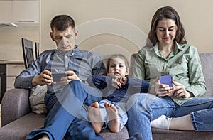 Family sit on the couch and hang out on their phones. Mom dad and daughter spend time with gadgets