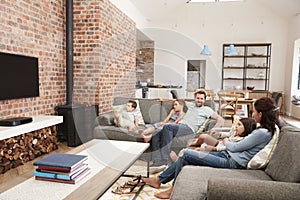 Family Sit On Sofa In Open Plan Lounge Watching Television