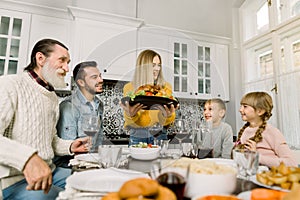 The family sits down for dinner on Thanksgiving. Young woman serves a festive turkey with a salad, grandfather, father