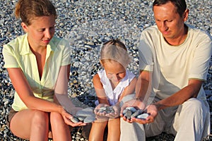 Family sits in pebbly beach and holding pebbles