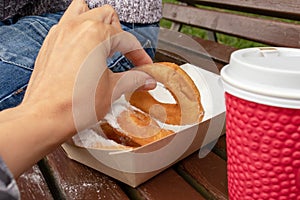 Family sitting on a bench in park and taking beignet pastries, donuts from a paper takeaway box and drinking coffee, street fast