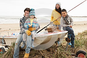 Family Sitting On Boat With Fishing Rod On Beach