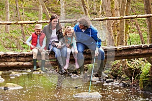 Family Sitting On Bridge Fishing In Pond With Net