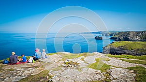 Family is sitting on a cliff at Tintagel castle in Cornwall, England with the Atlantic Ocean coastline