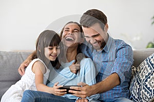 Family sitting on couch using smartphone watching video laughing