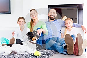 Family sitting with dog at living room floor fireplace