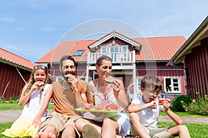 Family sitting in grass front of home eating water melon