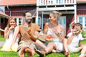 Family sitting in grass at house eating water melon