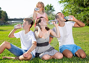 Family sitting on green lawn and drinking water