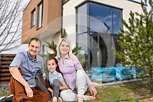 Family sitting on lawn in backyard, big modern house on background