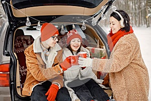 Family sitting in open car& x27;s trunk at winter park and drink a tea