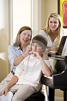 Family sitting on piano bench, mother teasing son