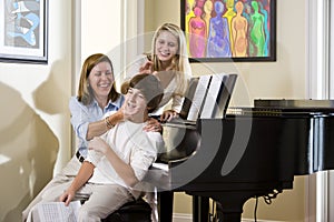 Family sitting on piano bench, mother teasing son