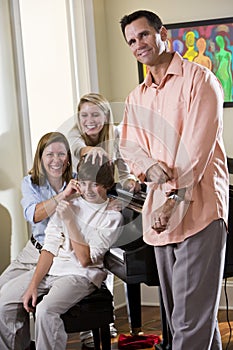 Family sitting on piano bench, mother teasing son