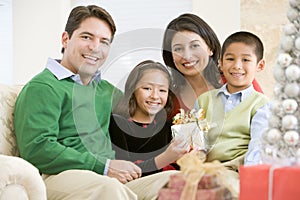 Family Sitting On Sofa Holding A Christmas Gift