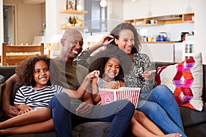 Family Sitting On Sofa At Home Eating Popcorn And Watching Movie Together