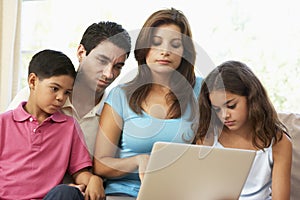 Family Sitting On Sofa At Home With Laptop