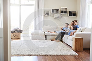 Family Sitting On Sofa At Home Watching TV Together