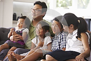 Family Sitting On Sofa At Home Watching TV Together