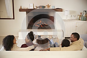 Family Sitting On Sofa In Lounge Next To Open Fire